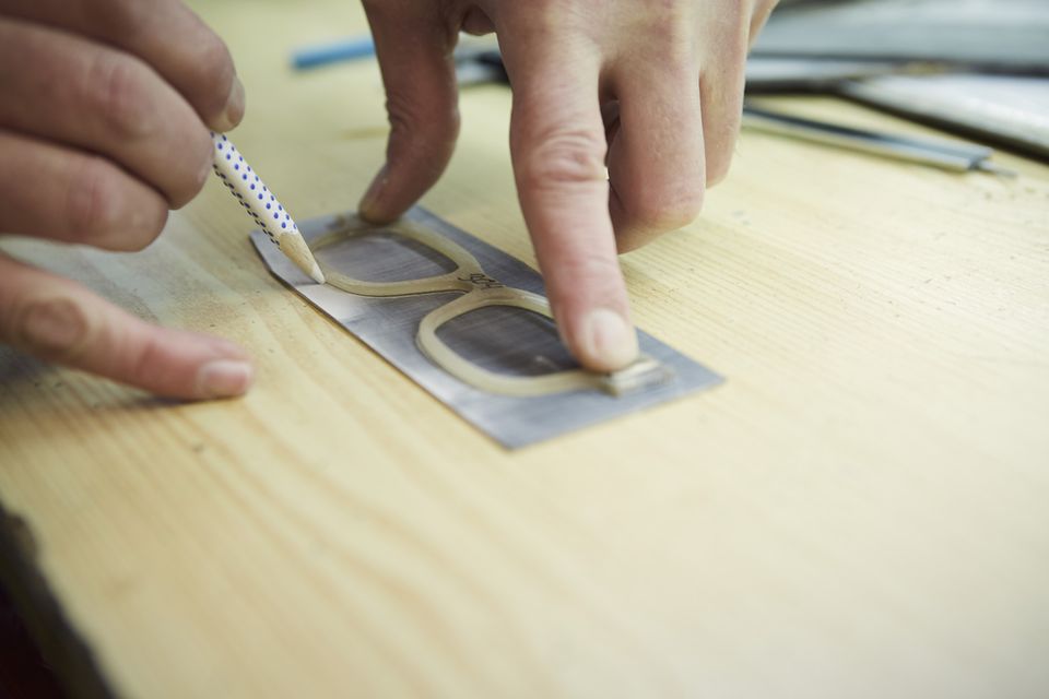 Mit einem Stift wird die Form einer Brillenfront entlang einer Schablone auf eine Platte übertragen